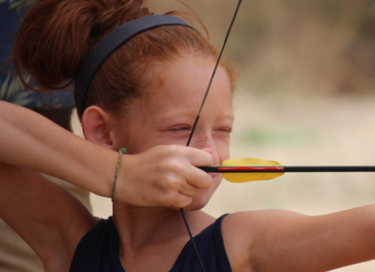 girl pulling aiming her bow getting ready to shoot a target